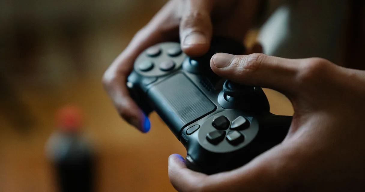 Mãos segurando um controle de console durante uma partida, ilustrando os jogos online no sofá